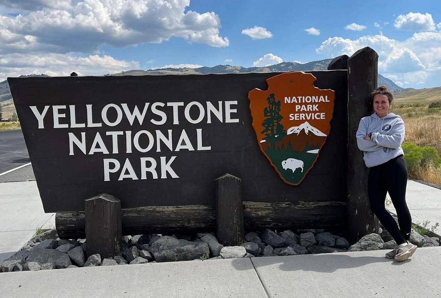 Woman standing on right in front of yellowstone national park sign