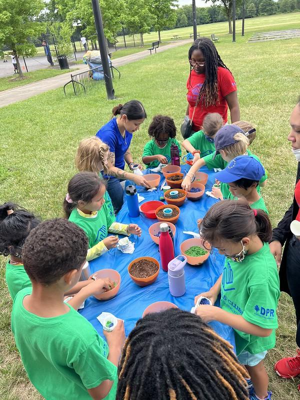 Youth surrounding a long blue table completing a hands-on seed bomb activity.