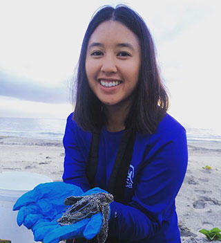 Diana Gu on beach holding sea turtle hatchling
