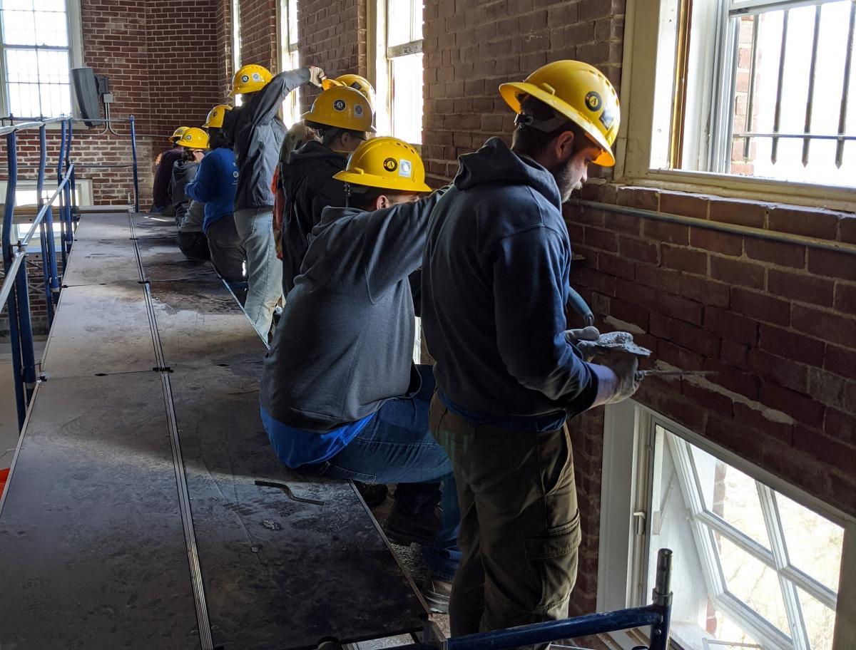 SCA members in yellow helmets working in brick building